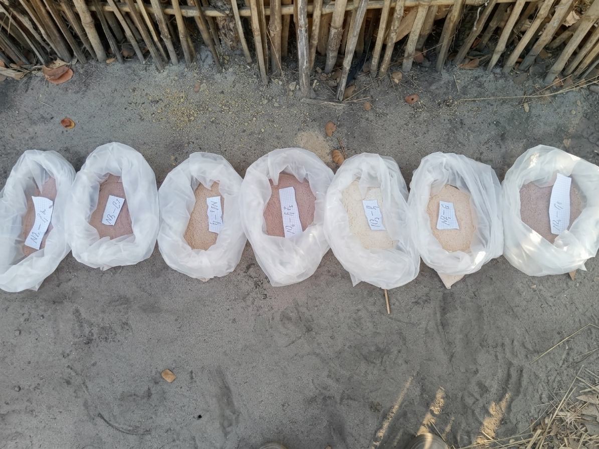 Sept sachets alignés au sol, contenant des échantillons de poudre/sable étiquetés avec de petits papiers.